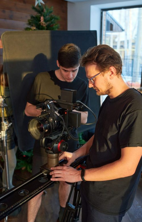 young-videographer-and-his-assistant-adjusting-options-of-video-camera